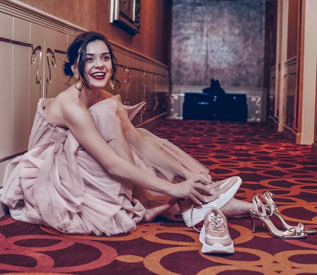 Аделина Сотникова в бежевом платье надевает кроссовки на ковре