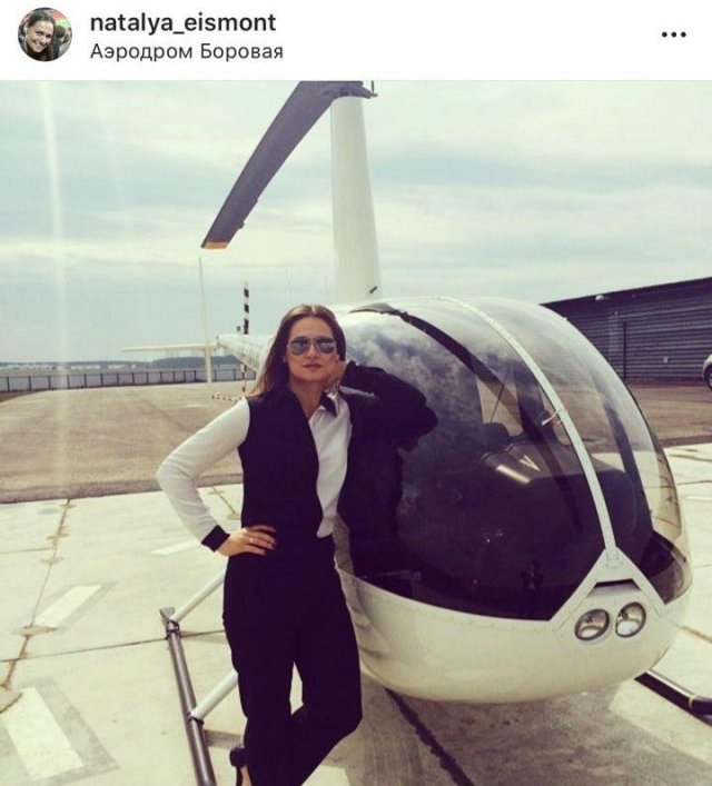 Наталья эйсмонт в белой рубашке и черном костюме на фоне белого вертолета