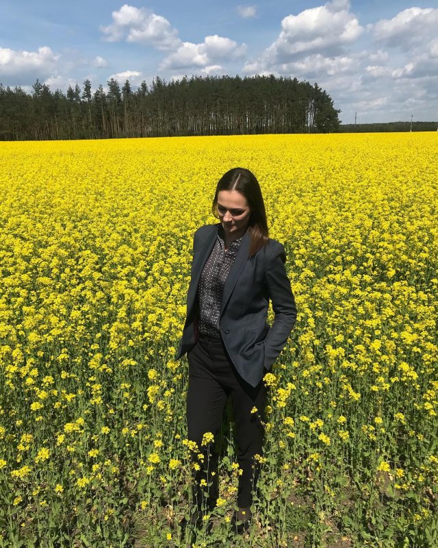 Наталья Эйсмонт в зеленом пиджаке и темных брюках в поле из желтых цветов