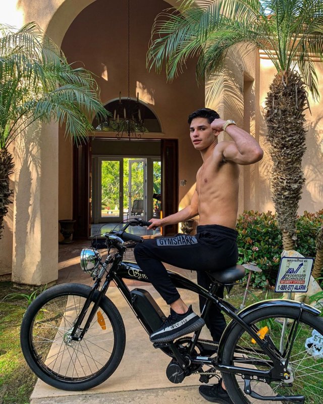Райан Гарсия в черных штанах на черном велосипеде напротив дома