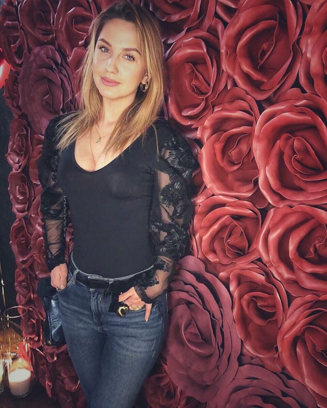 Элеонора Хабибулина на фоне цветов в черной кофте и джинсах