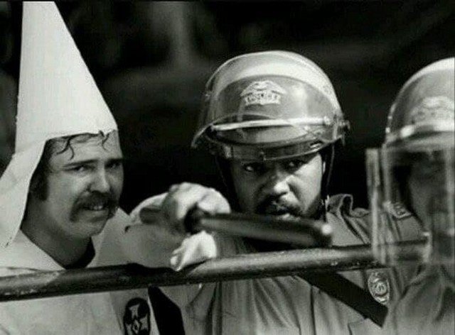 Чёрный полицейский защищает членов Ку-Клукс-Клана от протестующих, 1983 год.