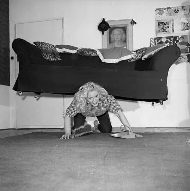 Английская цирковая силачка мисс Джоан Роудс поддерживает себя в форме занимаясь уборкой у себя в квартире, 1958 год