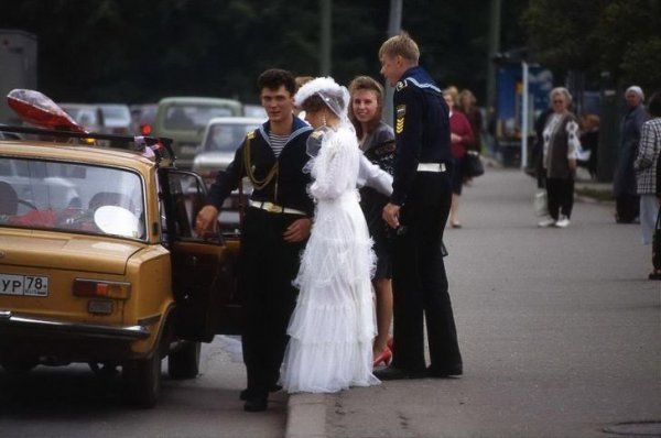 Жених и невеста садятся в машину, украшенную свадебной атрибутикой