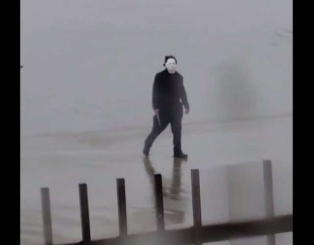 Человек в костюме Майкла Майерса, держа в руках нож, гуляет по улице и пугает местных жителей