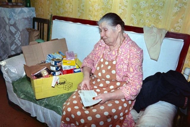 Пожилая женщина открывает коробку с продуктами и лекарствами из гуманитарной помощи, полученной от немецких организаций. Продовольственный кризис в России. 1990-е.
