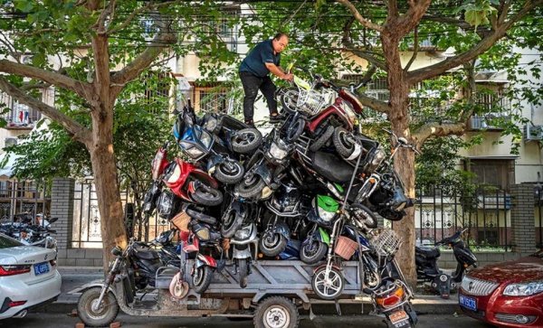 Мужчина складывает утилизированные электровелосипеды и скутеры на свой трёхколесный электрический велосипед для переработки, Пекин