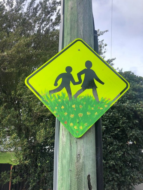 Дружелюбный пешеходный знак, на котором дети теперь бегут по зелёной лужайке