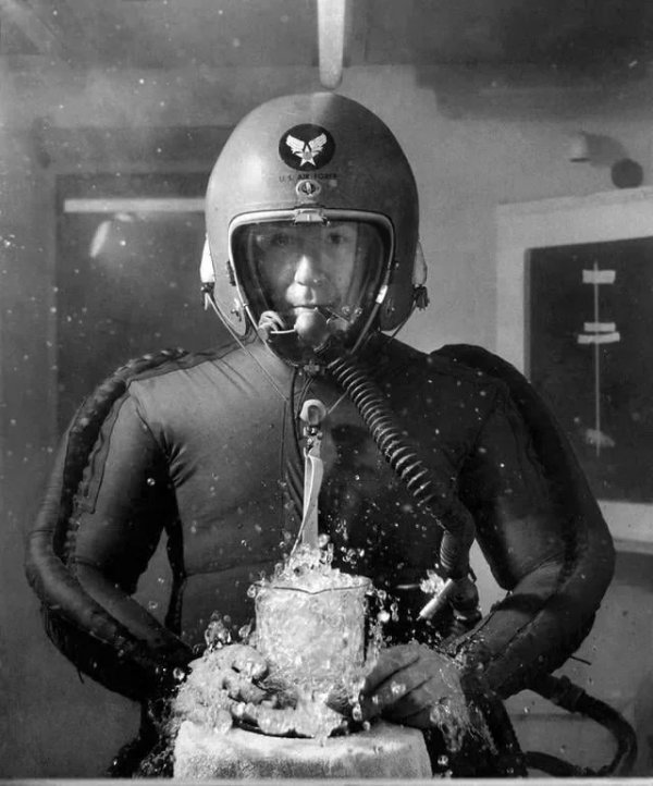 Человек в скафандре держит мензурку с кипящей водой. Он находится в вакуумной камере, имитирующей высоту 20 километров, 8 февраля 1953 год