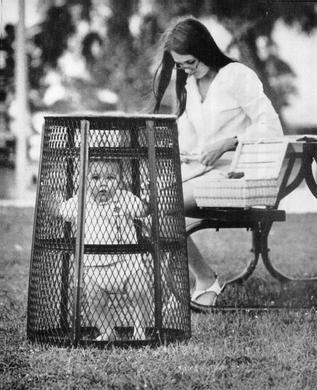 Мама использует мусорную корзину, чтобы удержать своего ребенка, пока она вяжет крючком, 1969 год