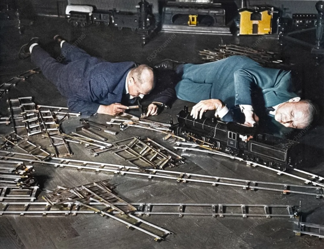 Два пожилых мужчины на полу в здании Общества игрушечных железных дорог. Один регулирует розетку небольшим молоточком, второй ремонтирует двигатель паровоза. Берлин, Германия, 1931 год. Два пожилых мужчины на полу в здании Общества игрушечных железных дорог. Один регулирует розетку небольшим молоточком, второй ремонтирует двигатель паровоза. Берлин, Германия, 1931 год.