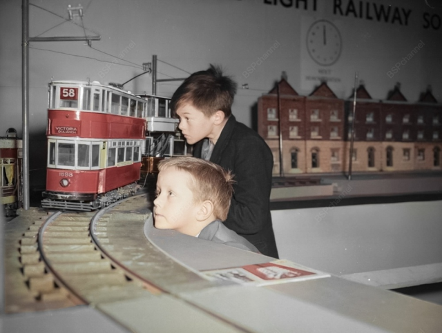 Ричард Ли и Раймонд Саттон наблюдают за миниатюрным трамваем, движущимся по рельсам на 5-й выставке моделей железных дорог в Центральном зале Вестминстера, Лондон, 1959 год.