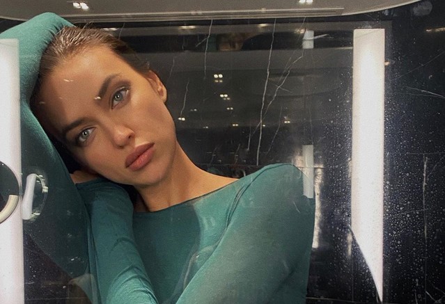 Ирина Шейк в ванной команте в зеленой кофте смотрит в зеркало